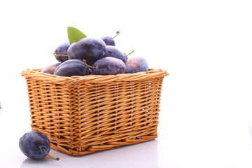 purple plums in a wicker basket on a white background