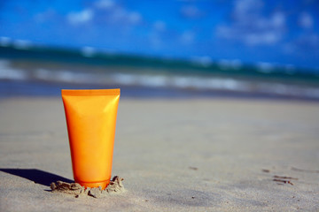 Sunscreen protection cream tubeon white sand at the beach. Tropical summer vacation concept
