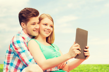 happy couple with tablet pc taking selfie outdoors