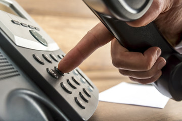 Closeup of male hand dialing a telephone number on black landlin