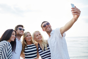 happy friends on beach and taking selfie