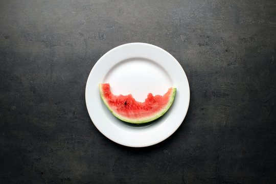 Watermelon slice with bites on white plate and dark kitchen table background