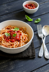 spaghetti with tomato sauce and Basil in a white bowl on a dark wooden surface