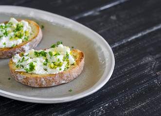 sandwiches with ricotta cheese, olive oil, pistachios and herbs is a delicious and healthy Breakfast or snack, on an oval plate on a wooden surface