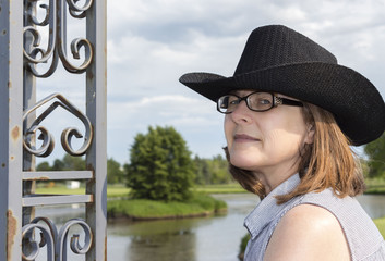 horizontal head shot image of a caucasian middle aged woman wearing glasses with brown shoulder length hair wearing a black cowboy hat with room for text.