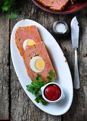 meat loaf with boiled egg, tomato sauce, coriander and parsley on a wooden table. rustic style.