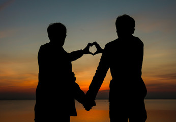 Gay couples making heart symbol on the romantic sunset.