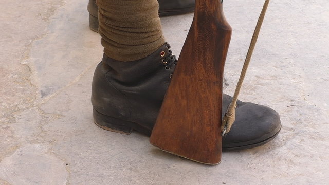Close up of around 1910 year or WW1 infantry soldier's feet wearing black boots and puttees and a rifle buttstock 
