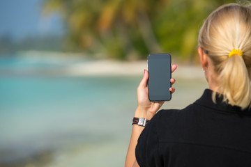 Woman hand showing a blank smart phone on the beach with the sea