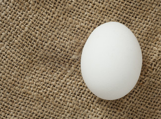 Białe jajko na tle jutowego worka