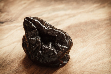 Single dried plum prune on wooden table