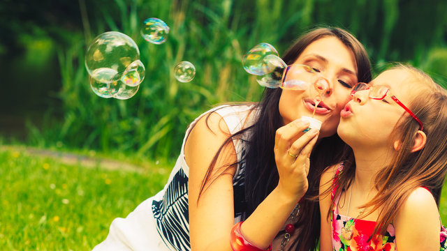 Mother and child blowing soap bubbles outdoor.