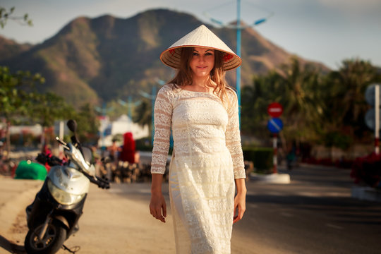 girl in Vietnamese dress and hat smiles by scooter