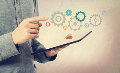 Young man pointing at gears over a tablet computer