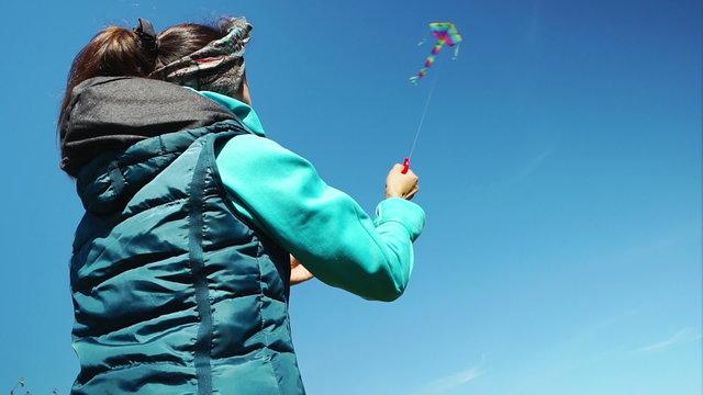 A young girl is launching a colorful kite in the blue sky. Back view
