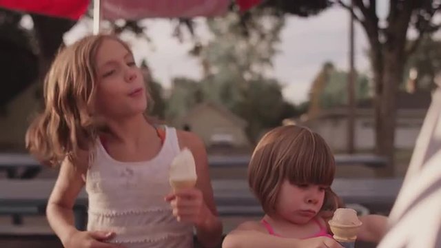 A girl wipes ice cream on her sister's nose at a picnic table
