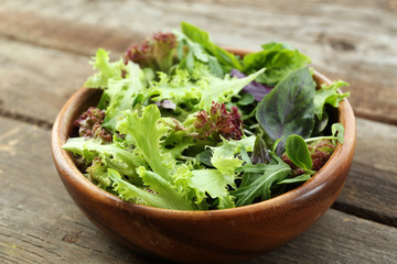 Fresh mixed green salad in bowl on wooden table close up