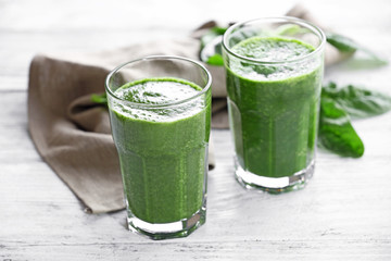 Glasses of spinach juice with napkin on wooden table, closeup