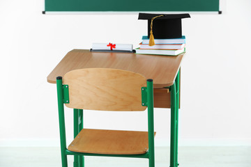 School desk with master hat, stack of books and diploma in classroom