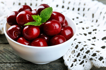 Sweet cherries with green leaves in bowl, on wooden background