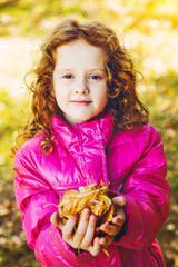 Curly girl in a red jacket with yellow autumn leaves in the hand