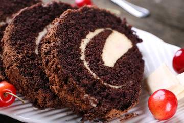 Delicious chocolate roll in white plate on wooden table, closeup