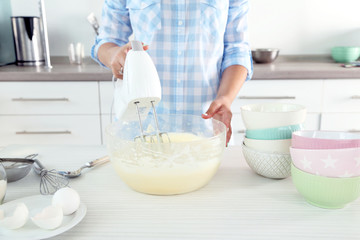 Young woman making rainbow cake in kitchen
