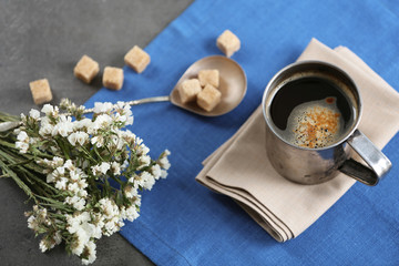 Metal cup of flavored coffee with lump sugar and flowers on table with napkin, closeup