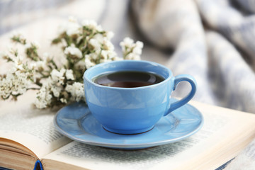 Blue cup of coffee with open book on sofa in room