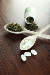 Dry medical cannabis and pills in spoons on table close up