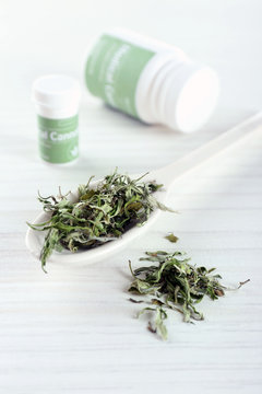 Bottle of medical cannabis with dry herbs in spoon on table close up