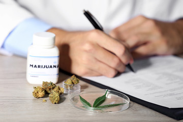 Doctor writing on prescription blank and bottle with medical cannabis on table close up