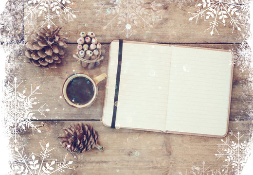 top image of open notebook with blank pages, next to pine cones and cup of coffee over wooden table. top image, glitter overly with snowflakes
