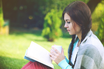 Fototapeta premium Young woman with book sitting on green grass outdoors