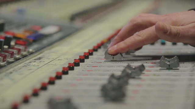 Close-up hands of sound engineer work with faders on mixer