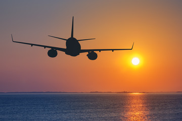Silhouette of passenger airplane flying on sunset