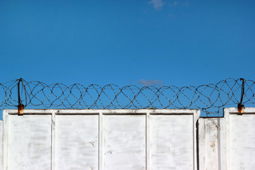 White concrete fence with barbed wire against a blue sky backgro