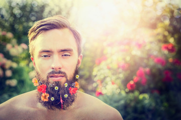 stylish man's face with a beard with flowers in his beard on natural bright-colored background