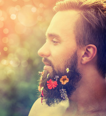 man's face in profile with a beard with flowers in his beard on natural background with bokeh