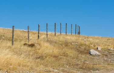 Guarded landscape - barrier with barbed wire against blue cloudless sky