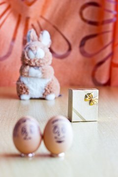 Painted easter eggs with man and woman smiling faces. Eggs on wedding rings. Blurred background with golden gift box and easter bunny. Conceptual funny image. Focus on gift box