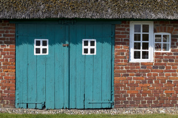 A Pattern of Windows. An old traditional farmhouse in Denmark, complete with thatched roof. The old windows form a repetitive pattern and the red brick contrasts with the teal wooden barn doors.