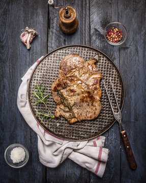 pork roast on an iron skillet with a napkin, fork, sauce, salt and pepper on rustic wooden background 