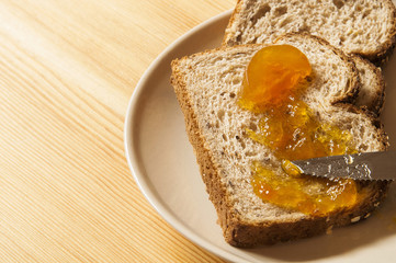 Two slices of whole wheat bread with homemade orange jam on a wooden table.