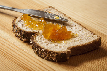 A single slice of whole wheat bread with homemade orange jam on a wooden table.