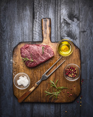 Raw fresh marbled beef steak with meat fork and seasonings  on rustic cutting board over blue wooden background