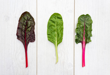 Three leaves of fresh swiss chard on a white table