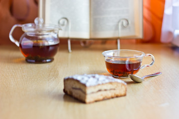 Still life composition: morning tea in glass cup and teapot with sweet cake and reading book.Selective focus on cup and blurred background