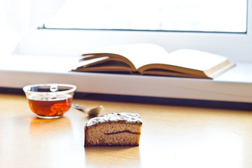 Still life composition: book tea cake. With selective focus and blurred background. Sunlight from window