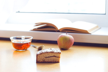Still life composition: book tea apple cake. With selective focus and blurred background. Sunlight from window